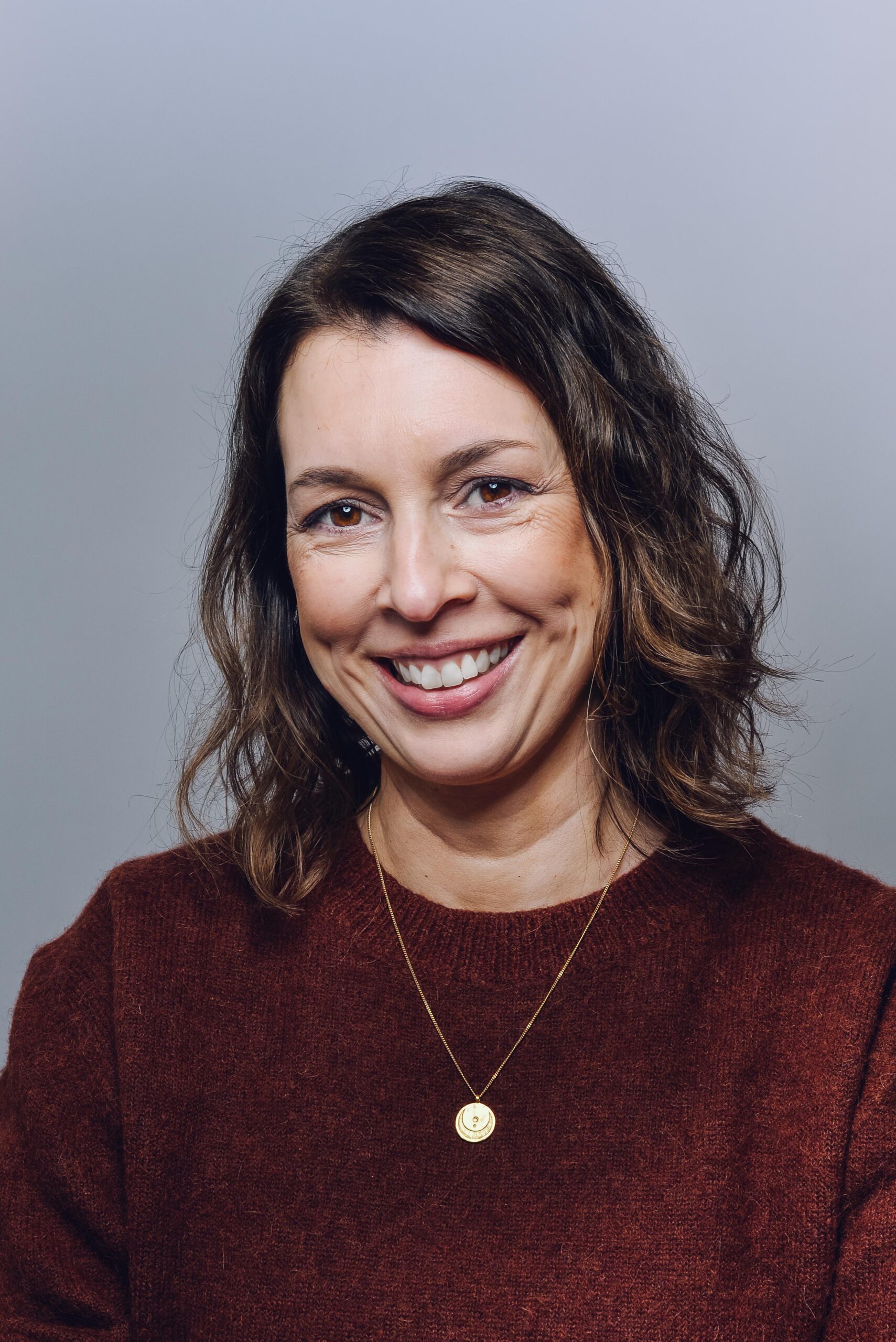 Profilbild von Evamaria Kalbantner, sie lächelt, hat braune Haare, einen rostbraunen Pullover und eine goldene Kette um.